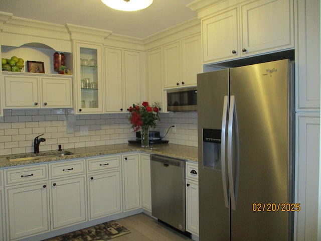 kitchen featuring light stone counters, stainless steel appliances, backsplash, glass insert cabinets, and a sink