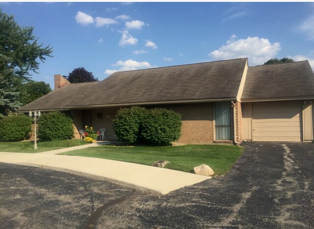 ranch-style house with an attached garage, brick siding, driveway, a chimney, and a front yard