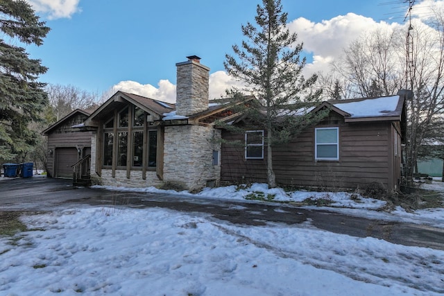 snow covered property featuring stone siding, a chimney, and an attached garage