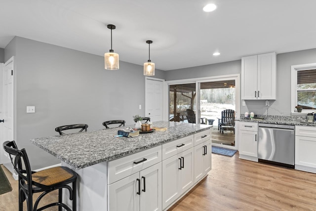 kitchen with light wood-style floors, white cabinets, stainless steel dishwasher, and a kitchen breakfast bar