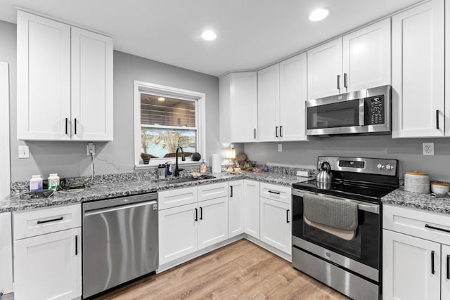 kitchen with light stone counters, light wood-style flooring, a sink, white cabinets, and appliances with stainless steel finishes