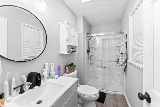 full bathroom featuring a textured ceiling, toilet, wood finished floors, vanity, and a shower stall