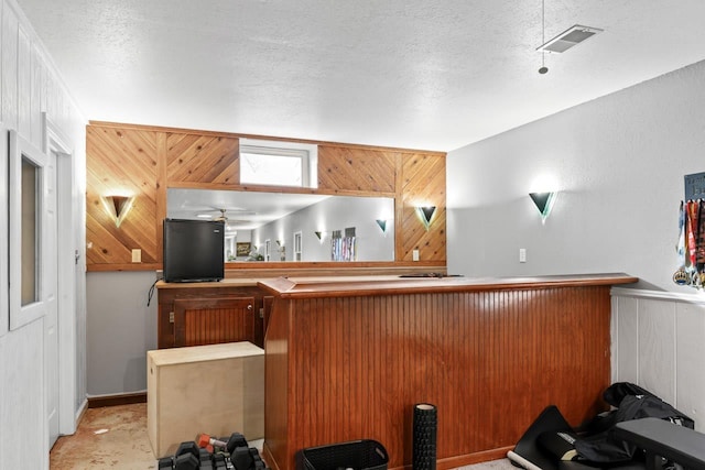 bar with a textured ceiling, wood walls, and visible vents