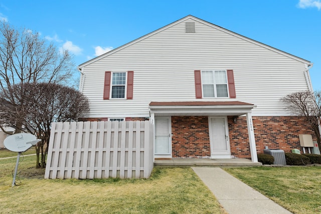 traditional home featuring brick siding, a front lawn, central AC unit, and fence