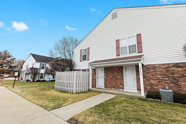 view of front of house with a front yard, brick siding, fence, and central AC