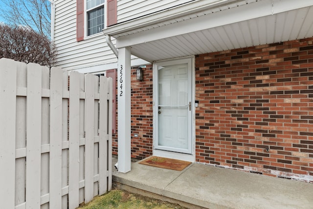 doorway to property with brick siding and fence