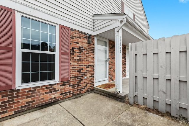 doorway to property featuring brick siding and fence