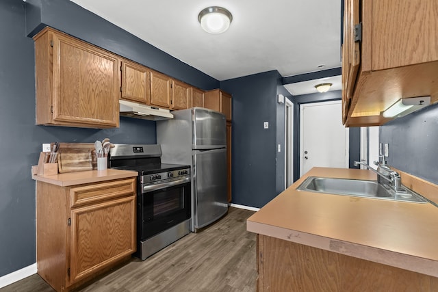 kitchen featuring under cabinet range hood, a sink, light wood-style floors, light countertops, and appliances with stainless steel finishes