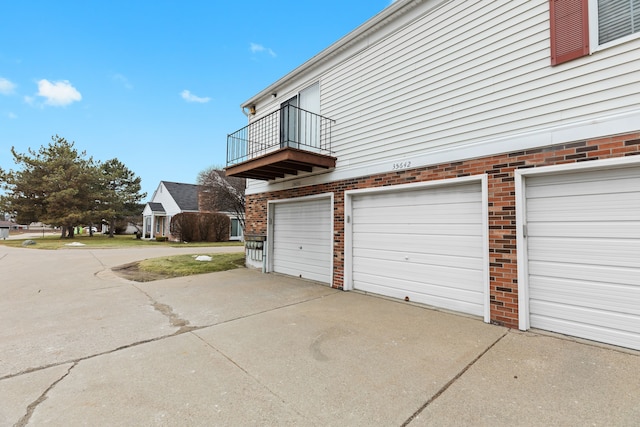 view of side of home featuring a garage, concrete driveway, brick siding, and a balcony