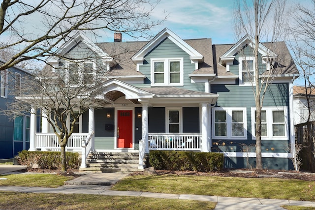 view of front facade featuring a shingled roof, a chimney, a front lawn, and a porch