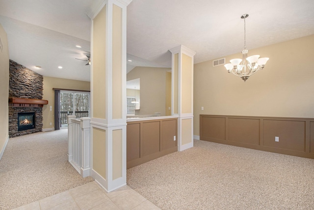 kitchen with a stone fireplace, a decorative wall, light carpet, ceiling fan with notable chandelier, and visible vents