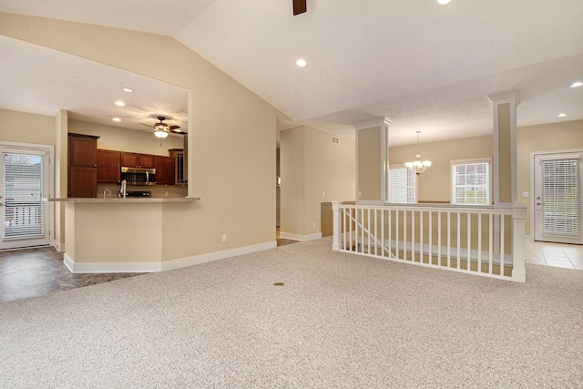 unfurnished room featuring ceiling fan with notable chandelier, vaulted ceiling, light carpet, and baseboards