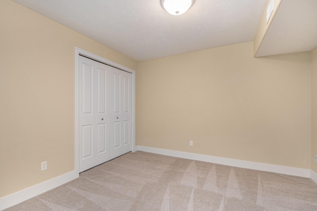 unfurnished bedroom with light carpet, a closet, a textured ceiling, and baseboards