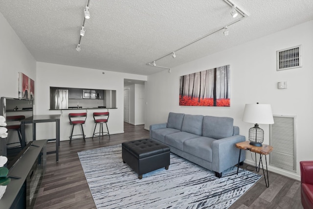 living area featuring track lighting, visible vents, dark wood-type flooring, and a textured ceiling