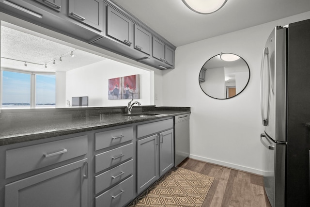 kitchen featuring baseboards, appliances with stainless steel finishes, wood finished floors, gray cabinetry, and a sink