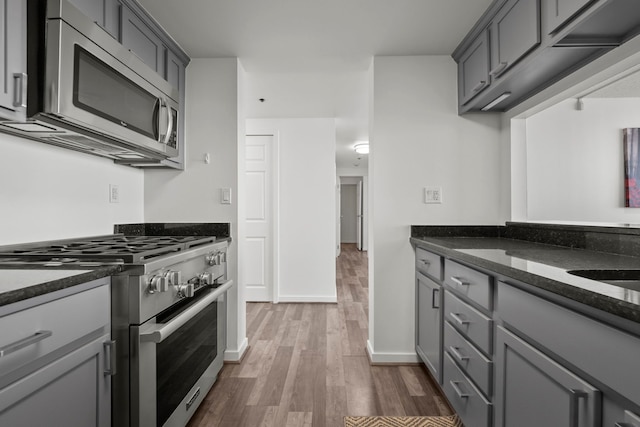 kitchen featuring appliances with stainless steel finishes, dark stone counters, dark wood-type flooring, and gray cabinetry