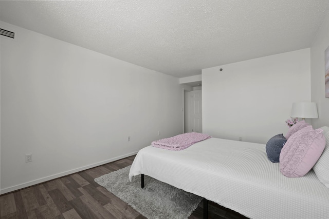 bedroom with a textured ceiling, dark wood-style flooring, visible vents, and baseboards