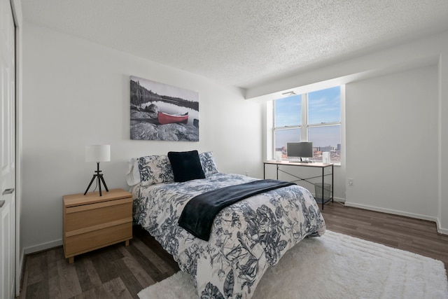 bedroom with dark wood-style flooring, a textured ceiling, and baseboards