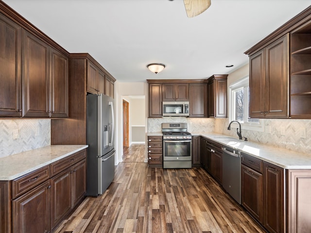 kitchen featuring open shelves, a sink, dark brown cabinetry, dark wood-type flooring, and appliances with stainless steel finishes