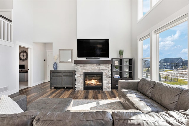 living room featuring a towering ceiling, a fireplace, baseboards, and wood finished floors