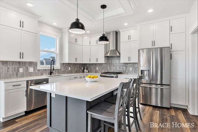 kitchen with dark wood finished floors, wall chimney exhaust hood, appliances with stainless steel finishes, a kitchen breakfast bar, and a sink