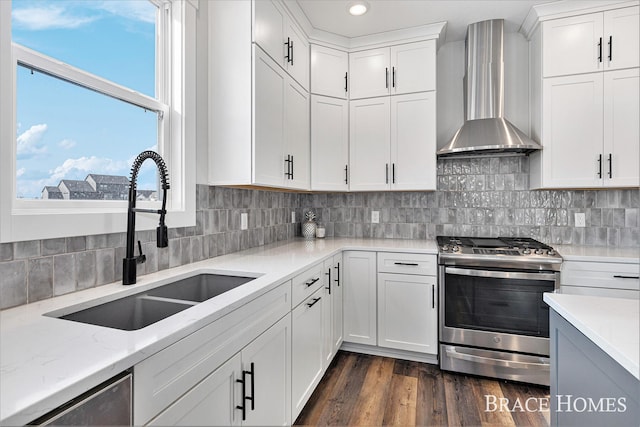 kitchen featuring light stone counters, stainless steel appliances, dark wood-type flooring, a sink, and wall chimney exhaust hood