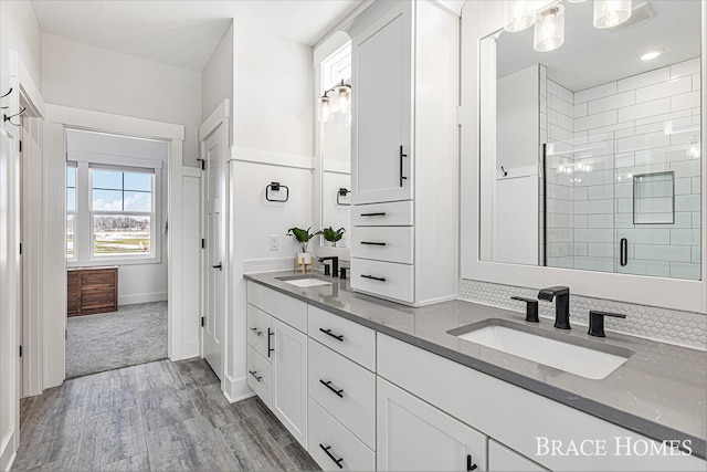 full bathroom with double vanity, a shower stall, a sink, and wood finished floors