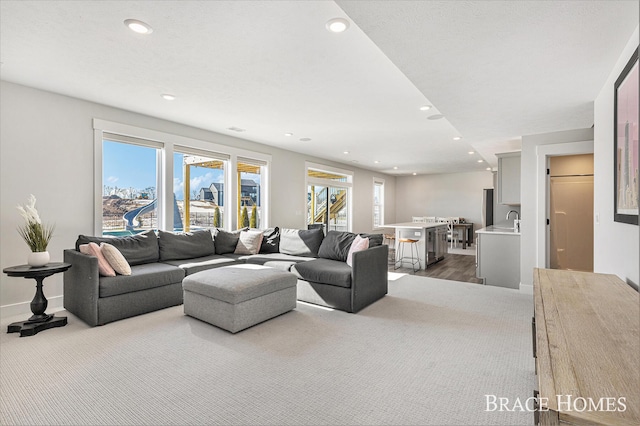 carpeted living room with a healthy amount of sunlight, baseboards, a sink, and recessed lighting