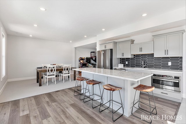 kitchen with light wood finished floors, a breakfast bar area, stainless steel appliances, tasteful backsplash, and gray cabinets