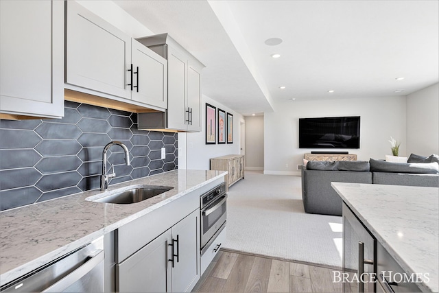 kitchen featuring light stone counters, a sink, appliances with stainless steel finishes, light wood finished floors, and tasteful backsplash