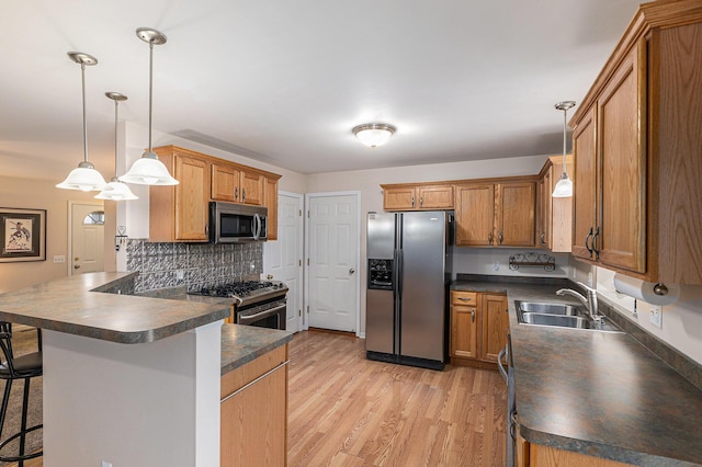 kitchen featuring stainless steel appliances, dark countertops, light wood-style floors, a sink, and a peninsula