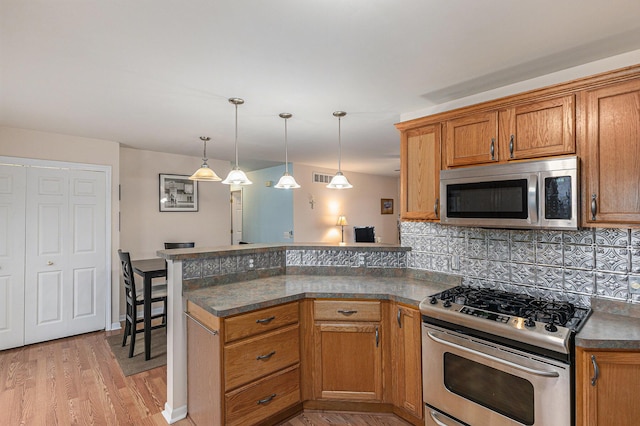 kitchen with stainless steel appliances, dark countertops, backsplash, brown cabinetry, and a peninsula