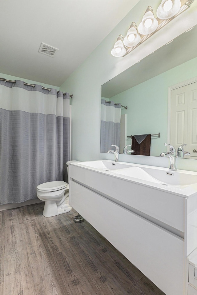 bathroom with visible vents, a shower with shower curtain, toilet, wood finished floors, and vanity