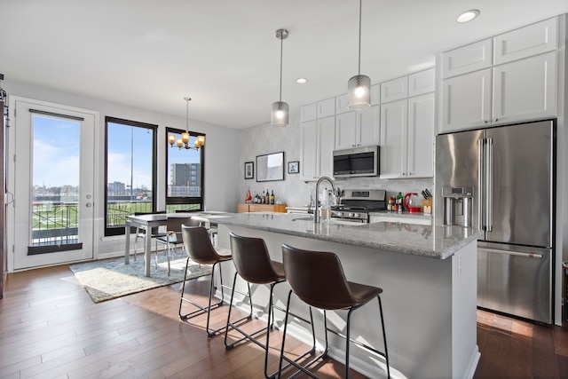 kitchen with an island with sink, appliances with stainless steel finishes, dark wood finished floors, and a kitchen breakfast bar