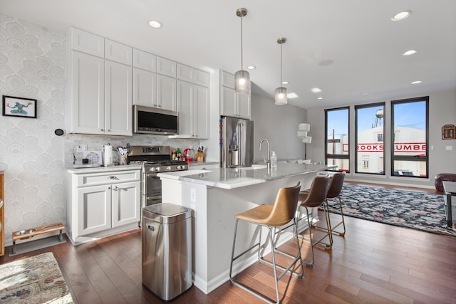 kitchen with dark wood-style floors, stainless steel appliances, recessed lighting, a kitchen bar, and wallpapered walls