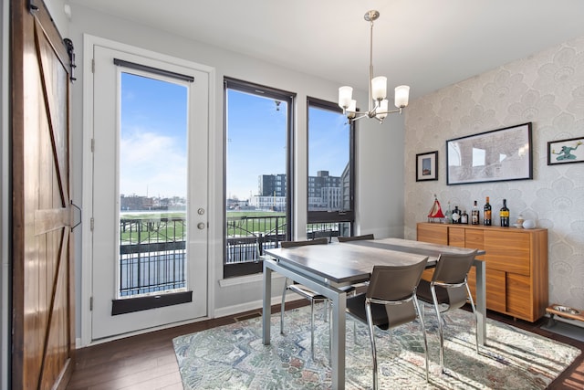 dining room with a city view, a barn door, wood finished floors, a chandelier, and wallpapered walls