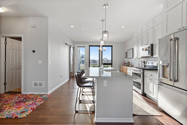 kitchen featuring visible vents, a barn door, appliances with stainless steel finishes, a kitchen island with sink, and white cabinets