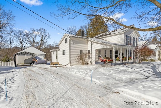 snow covered property featuring a chimney, a porch, and a detached carport