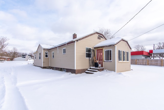 snow covered back of property with a chimney and fence