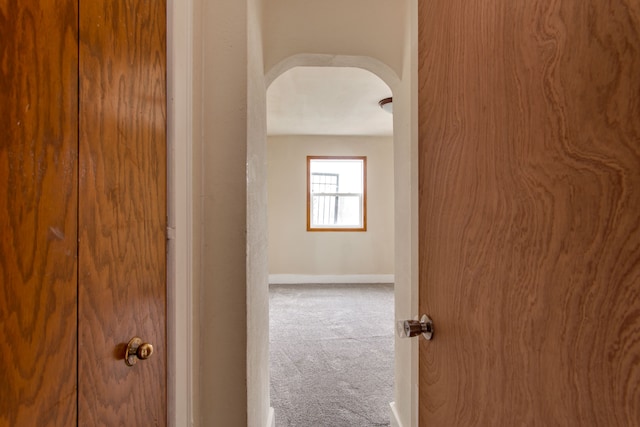 hallway featuring arched walkways, carpet, and baseboards