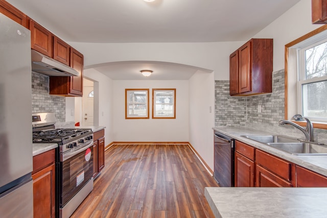 kitchen featuring under cabinet range hood, stainless steel appliances, wood finished floors, a sink, and light countertops