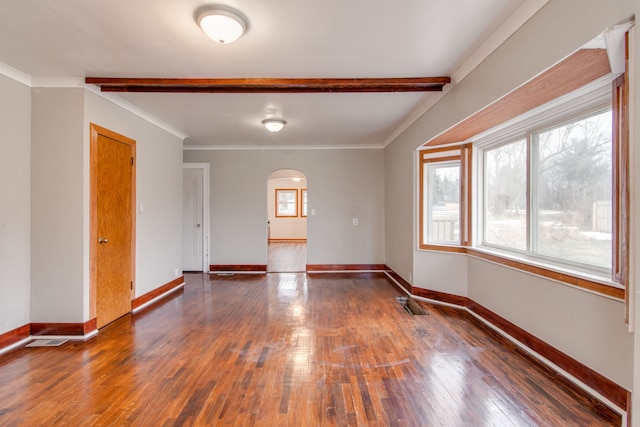 empty room with a wealth of natural light, arched walkways, wood-type flooring, and baseboards