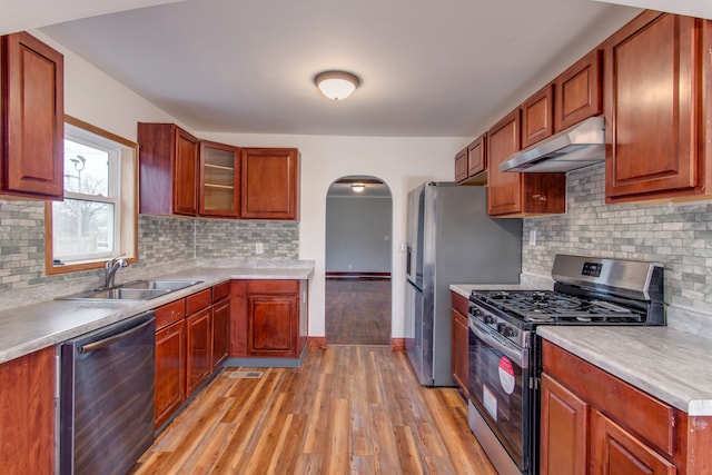 kitchen featuring arched walkways, appliances with stainless steel finishes, a sink, light wood-type flooring, and under cabinet range hood