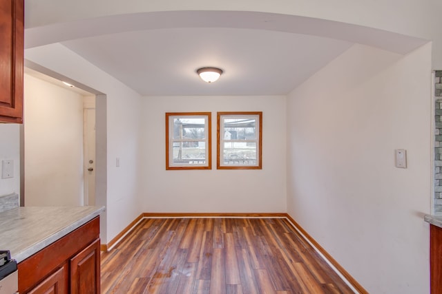 unfurnished dining area with baseboards, arched walkways, and dark wood-style flooring