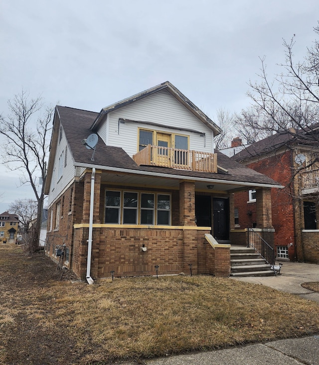 view of front of property featuring a balcony, a shingled roof, and brick siding