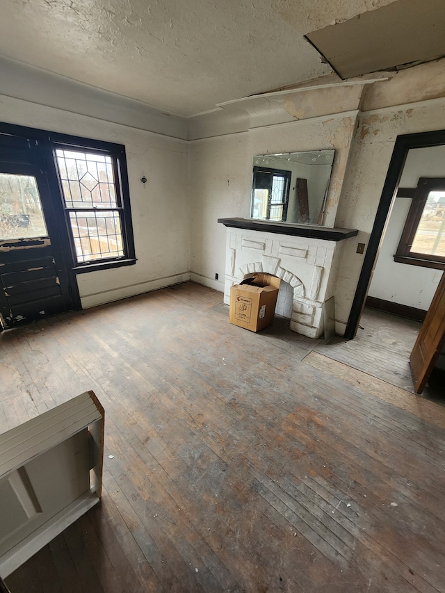 unfurnished living room featuring a textured ceiling, baseboards, and hardwood / wood-style floors