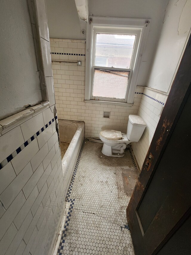 bathroom with tile walls, a bathing tub, toilet, and tile patterned floors