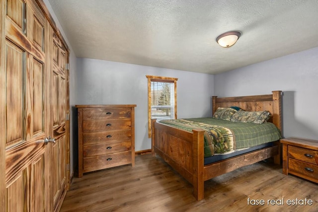 bedroom with a textured ceiling, baseboards, and wood finished floors