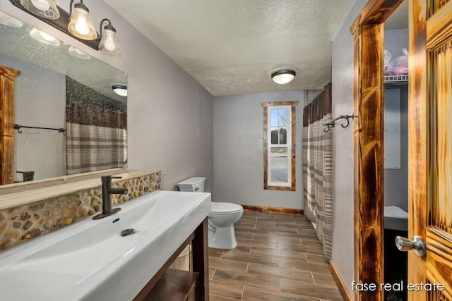 bathroom with a textured ceiling, toilet, wood finish floors, vanity, and baseboards