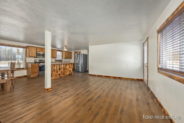 unfurnished living room with a wealth of natural light, dark wood finished floors, a textured ceiling, and baseboards